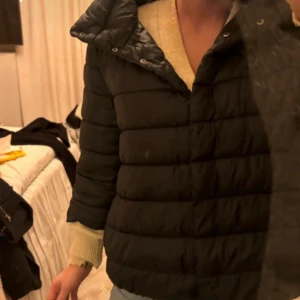 Svart pufferjacka - Säljer en svart pufferjacka som är perfekt för kyliga dagar. Jackan har en quiltad design och trekvartsärm. Den är både stilren och varm, vilket gör den idealisk för höst och vinter.