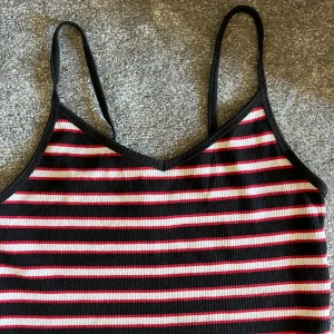 Randig linne från FB Sister - Säljer ett snyggt randigt linne från FB Sister i storlek M. Linnet har smala axelband och är perfekt för sommaren. Det är randigt i svart, rött och vitt och har en ribbad struktur. Passar perfekt till både vardag och fest!