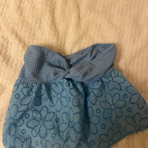 Blå kjol med blommigt mönster - Säljer en superfin blå top med ett blommigt mönster. Toppen har en söt knutdetalj och är perfekt för sommardagar. Materialet känns lätt och luftigt, vilket gör den idealisk för varma väder. Passar perfekt till en enkel topp och sandaler för 