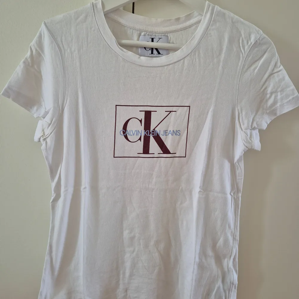 Vit T-shirt med vinröd och ljusblå tryck från Calvin Klein. Slim modell. Stretchbar. Storlek S. 100% bomull. . T-paidat.
