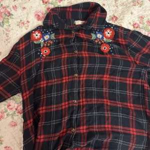 Rutig skjorta med broderade blommor - Blå och röd skjorta med fina broderade blommor på. 