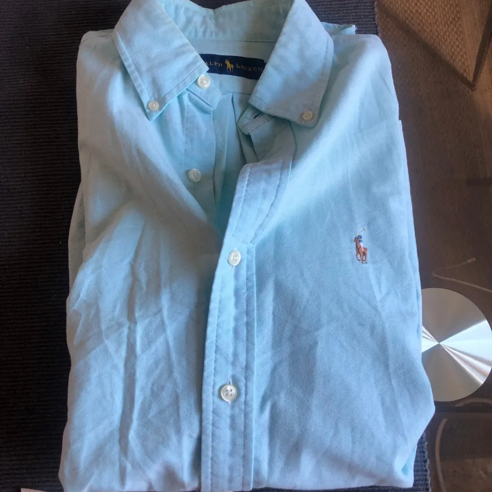 Säljer en oanvänd Ralph Lauren Oxford skjorta i storlek Medium.  Färgen är turkos. Den är givetvis äkta och köpt på NK i Stockholm. Finns QR kod att scanna men dock inget kvitto.  Köptes i våras.   Passform slim fit. . Skjortor.