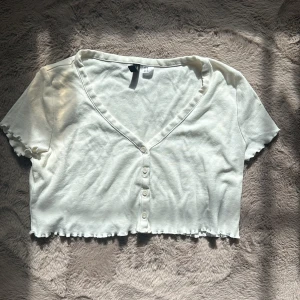 Vit topp - Kort vit topp med volanger i sömmarna och knappar fram, skick 6/10