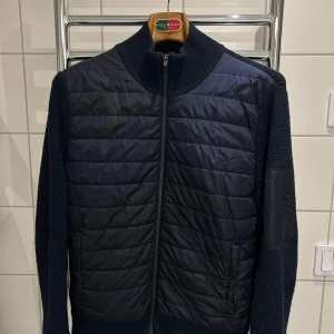 J.Lindeberg cardigan - En marinblå snygg cardigan från j.lindeberg. Börjar bli nopprig men går enkelt att fixa. Inga andra skador, tror nypris var 2200 när jag köpte den.