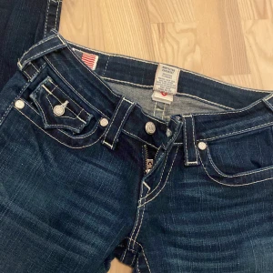True religion jeans  - Snygga mörkblå trueys jeans med vita sömmar och knappar med pärlor på.  I strl 26 och Inga skador förutom att jag har sprättat upp ena benet som man kan se på sista bilden och pris kan diskuteras❤️