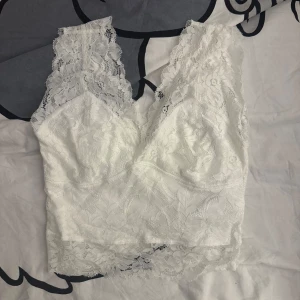 Vit spetslinne - Säljer ett vackert vitt spetslinne. Linnet har en v-ringad design med spetsdetaljer och ärmlös stil. Perfekt för att lägga till en romantisk touch till din outfit.