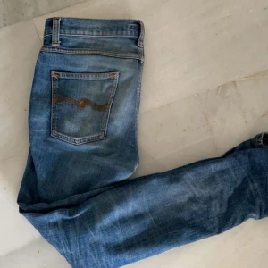 Nudie jeans - Snygga blå jeans med en broderad detalj på bakfickan. De har en slim passform och är perfekta för en stilren look. Stl 31/32 