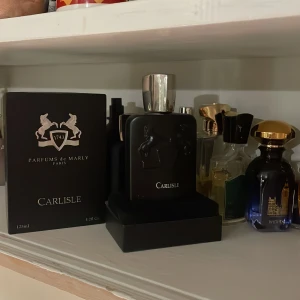 Parfym Carlisle från Parfums de Marly 110 ml återstår  - Elegant parfymflaska från Parfums de Marly, modell Carlisle. Flaskan är svart med en stilren design och har en kapacitet på 125 ml. Förpackningen är också svart med guldiga detaljer och logotypen med två hästar. Perfekt för den som söker en lyxig doftupplevelse.