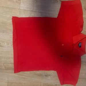 Röd pikétröja från Polo Ralph Lauren - Snygg röd pikétröja från Polo Ralph Lauren med klassisk krage och knappar framtill. Perfekt för en stilren look.