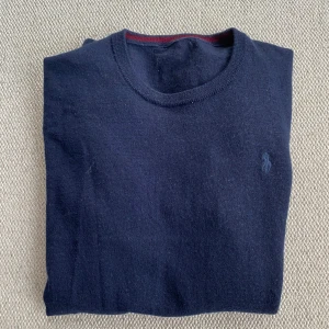 Mörkblå tröja från Ralph Lauren - Säljer en stilren mörkblå tröja från Ralph Lauren med rund halsringning. Tröjan är gjord av merino ull och är i ett fint skick. Det är endast en liten defekt då det är ett litet hål vid nacken. Skick 7/10. Storlek S/XS tröjan är lite för liten för mig som är 175. Hör av dig vid minsta fundering!💭 