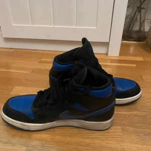 Nike Air Jordans i svart och blått - Säljer ett par Nike Air Jordans i svart och blått. Skorna har en klassisk design med snörning och en hög siluett. Perfekta för sneaker-entusiaster som vill ha en stilren look. Inte använda mycket alls, ingår crease skydd. Köpta för 2000