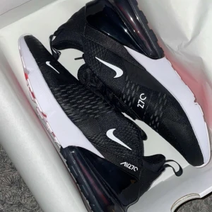 Svarta Nike Air Max 270 - Snygga och moderna svarta Nike Air Max 270 sneakers med vit sula och ikonisk Nike-logga. Perfekta för både träning och vardag med bekväm passform och stilren design.