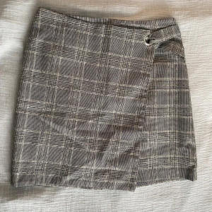 Rutig kjol med omlott - Snygg rutig kortkjol med omlott-design och en cool ringdetalj i midjan. 