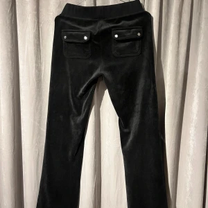 Svarta byxor från Juicy Couture - Snygga svarta byxor från Juicy Couture i mjukt material med broderad logga. Byxorna har fickor med knappar baktill. Knappt använda!