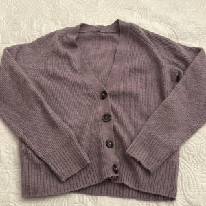 Lila kofta från Lindex - Säljer en mysig lila kofta från Lindex Kids i storlek 170, däremot tycker jag passformen är lik storlek M. Koftan har en v-ringad design med stora knappar framtill och ribbade muddar vid ärmslut och nederkant. 