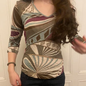 Mönstrad topp med trekvartsärm - Säljer en unik topp med ett färgglatt geometriskt mönster i brunt, beige, blått och vinrött. Toppen har en v-ringad hals och trekvartsärmar. Jag köpte den second hand!