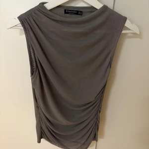 Grå ärmlös topp från Stradivarius - Snygg grå ärmlös topp från Stradivarius med draperade detaljer på sidorna. Perfekt för en stilren look. Tillverkad i ett lätt och luftigt material. Aldrig använd! 