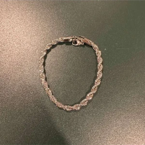 Silverfärgat armband med tvinnad design - Elegant silverfärgat armband med en vacker tvinnad design. Perfekt för att ge en stilren touch till din outfit. Armbandet har en säker låsning och passar de flesta handleder.