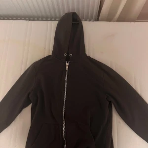 Svart hoodie med dragkedja  - Säljer en stilren svart hoodie i storlek M. Den är tillverkad av 100% bomull och har en praktisk dragkedja framtill samt en rymlig huva. Perfekt för en avslappnad look.