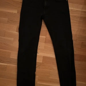 Lee Rider svart 32/32 - The super clean black finish has a designer vibe that keeps things minimal. These will age beautifully, with crease lines slowly coming through over time as they mould to you.  The black stitching keeps up the minimal look, while silver buttons and rivets add just a touch of contrast.   https://eu.lee.com/se-en/shop/jeans/men/rider-slim-straight/rider-in-clean-black-L701HFAE.html?merchCategory=c030000&_gl=1*1yd0ehd*_up*MQ..*_ga*NzI5NzgwNzkzLjE3MzYwMTg5NTQ.*_ga_QXKL6FH5D6*MTczNjAxODk1NC4xLjEuMTcz