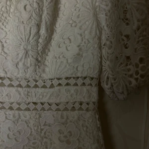 Vit spetsklänning med puffärmar - Min studentklänning!! vit klänning i spets med blommigt mönster och puffiga kortärmar. Den har en fyrkantig urringning och dekorativa band i midjan och sitter perfekt. Perfekt för studenten! dock lite färgad på framsidan pga färgbomb men går enkelt bort med en tvätt (gick bort på min andra klänning) så det är inget problem. Kom privat för tydligare bilder på hur den sitter!! 