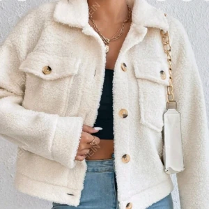 Vit teddyjacka med knappar - Snygg vit teddyjacka från SHEIN med knappar framtill och två bröstfickor. Jackan har en klassisk krage och är perfekt för kyligare dagar. Den är både stilren och mysig.