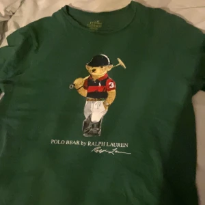Grön t-shirt med Polo Bear från Ralph Lauren - Snygg grön t-shirt från Ralph Lauren med det ikoniska Polo Bear-trycket på framsidan..