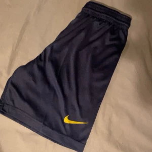 Svarta träningsshorts från Nike - Snygga svarta träningsshorts från Nike med gul logga. Perfekta för sport och träning med elastisk midja för bekväm passform.