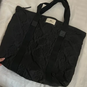 Svart shoppingväska från Day Birger et Mikkelsen - Snygg svart shoppingväska från Day Birger et Mikkelsen med broderade detaljer. Väskan har två långa handtag och en praktisk dragkedja upptill. Perfekt för att bära med sig allt man behöver under dagen.