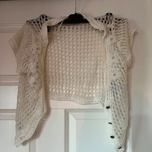 Vit virkad topp från Cream - Säljer en vit stickad bolerotopp från Cream. Den har ett öppet nätmönster och korta ärmar med dekorativa knappar framtill.  Så så söttttt