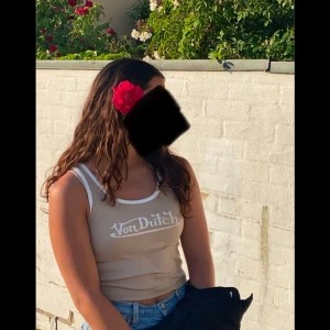 Beige linnetopp från Von Dutch - Snygg beige linnetopp från Von Dutch med vit textlogga på bröstet. Toppen har smala axelband och en klassisk rund halsringning. Perfekt för varma sommardagar!