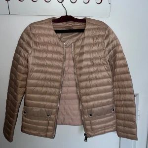 Ljusrosa pufferjacka från Ralph Lauren - Snygg ljusrosa pufferjacka från Ralph Lauren med dragkedja framtill. Jackan har en quiltad design och är perfekt för våren! Den har långa ärmar och två fickor med knappar. 