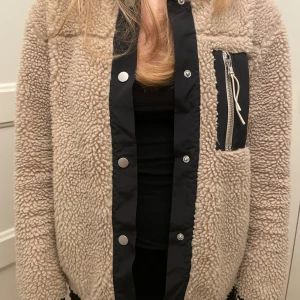 Beige teddyjacka med svarta detaljer - Mysig beige teddyjacka med svarta detaljer och dragkedja, bra skick!