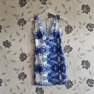 Vit och blå klänning från NLY One - Säljer en superfin vit och blå klänning från NLY One i storlek S. Den har ett vackert blommigt mönster och en djup v-ringning. Klänningen är ärmlös och har en tight passform som framhäver figuren. Perfekt för sommarens fester! Materialet är 92% polyester och 8% elastan, vilket gör den både bekväm och stretchig.