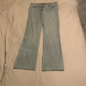 Ljusblå jeans med bootcut - Säljer ett par ljusblå jeans med bootcut-stil. De är tillverkade i 100% bomull och gjorda i Portugal. Jeansen har en cool, lite sliten look med ljusa detaljer längs benen. Perfekta för en avslappnad vardagsstil!