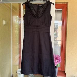 Klänning från Soaked in Luxury - Säljer en elegant klänning från Soaked in Luxury i storlek XS. Klänningen är ärmlös och har en vacker v-ringning med dekorativa knappar. Den är tillverkad i ett mjukt och bekvämt material, perfekt för festliga tillfällen. Klänningen har en dragkedja på baksidan för enkel på- och avklädning. Passar perfekt för både sommar och höst!