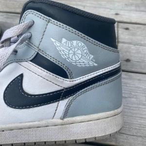 Air Jordan 1 Mid Light Smoke Grey Anthracite - Säljer ett par äkta Nike Air Jordan sneakers i grått och vitt. Skorna har en klassisk design med snörning och Nike-loggan på sidan. De är i välanvänt skick därav priset men fortfarande snygga och bekväma. Köpta för 2500kr, skriv vid frågor