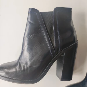 Svarta stövletter med klack - Säljer ett par mörkblåa stövletter från Zara med hög klack, 11cm.. De är i bra skick och har en stilren design som passar perfekt till både vardag och fest. Skorna har en bekväm passform och är lätta att ta på och av.