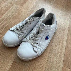 Vita sneakers från Champion - Säljer ett par vita sneakers från Champion i storlek 39. Skorna är välanvända med synliga tecken på slitage, särskilt på hälen. Men fungerar fortfarande riktigt bra☺️