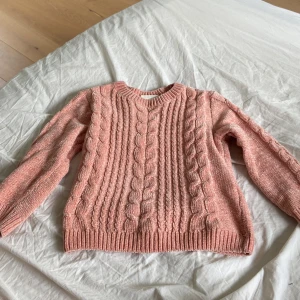 Rosa stickad tröja från KappAhl - Säljer en superfin rosa stickad tröja från KappAhl. Den är i storlek 122/128 och har ett snyggt flätmönster på framsidan. Tröjan är långärmad och perfekt för höst och vinter. Den är i bra skick och väldigt mysig att ha på sig. Perfekt för att hålla sig varm och stilig under de kallare månaderna! 💖