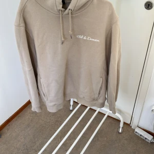 Beige hoodie med text - Säljer en beige hoodie med texten 'Club de Demain' broderad på bröstet. Den är supermysig och perfekt för höst och vinter. Hoodien har en normal passform och är gjord av mjukt material. Den har en stor ficka på magen och en justerbar huva med snören. Perfekt för att hålla sig varm och bekväm!