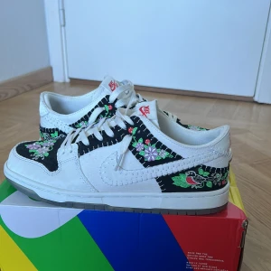 SB Dunk N7 (unika) - Säljer ett par snygga Nike Dunk sneakers i storlek 43. Skorna är vita med svarta detaljer och har ett coolt blommigt mönster på sidorna och tån. De är i bra skick. Kommer med originalkartong. Priset kan diskuteras. Vid snabb affär 650kr 
