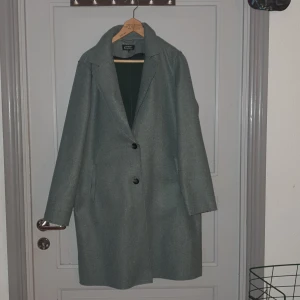 Grå kappa från ONLY - Säljer en stilren grå/grön kappa från ONLY i storlek M. Den har en klassisk design med två knappar framtill och långa ärmar. Perfekt för höst och vinter, och passar både till vardags och fest. Materialet känns mjukt och bekvämt, och kappan är i mycket bra skick. jag har aldrig andvänt den 