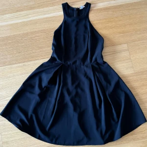 Svart ärmlös klänning - Klänningen har en tight passform upptill och en utsvängd kjol som ger en fin siluett. Klänningen är utskuren på skidorna. 