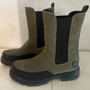 Gröna boots💚 - Säljer ett par snygga gröna boots i mocka med en robust sula ifrån märket Rieker. De har en cool design med svarta elastiska paneler på sidorna för enkel på- och avtagning. Perfekta för höst och vinter!🌨️🍃💚