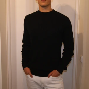 Svart stickad tröja - Säljer en stilren svart tröja som är perfekt för både vardag och fest. Tröjan har en normal passform och är långärmad. Den är i nyskick och har ribbade detaljer. Materialet är kashmir vilket gör den till en exklusiv och bekväm tröja. 