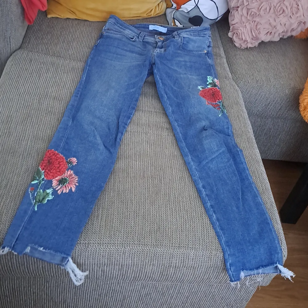 Säljer ett par snygga blå jeans med blommigt broderi på benen. De har en skinny passform och är i ett välanvänt skick. Perfekta för en casual look med en twist! De har en klassisk femficksdesign och en dragkedja med knapp framtill.. Jeans & Byxor.