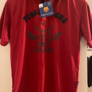 Piké Fc Barcelona - Piké i barnstorlek. Mörkröd med mörkblå krage. Aldrig använd. Prislapp kvar. Står stl 14 men ser liten ut.