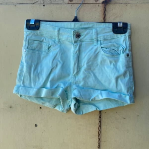 Ljusa turkosa shorts från H&M - Säljer ett par ljusa turkosa shorts från H&M. De är i en skön bomullsmix och har en normal passform. Shortsen har fickor både fram och bak samt en knapp och dragkedja framtill. Perfekta för sommardagar! 🌞