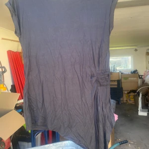Svart blus från Elitzia - Säljer en svart topp från Elitzia i storlek S. Toppen har en enkel och stilren design med korta ärmar och en asymmetrisk detalj på sidan. Perfekt för både vardag och festliga tillfällen!